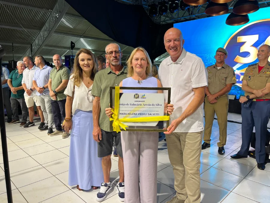 Prefeito Evandro Scaini entrega título de Cidadã Amiga do Arroio à empresária Mara Salvetti durante o aniversário de 30 anos de Balneário Arroio do Silva. Evento na Praça Central destaca o desenvolvimento económico e o turismo da região.