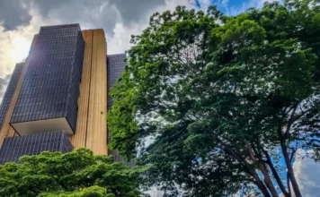 BC lança Protege+ para barrar abertura de contas fraudulentas Edifício sede do Banco Central do Brasil em Brasília, visto de baixo, ladeado por árvores.