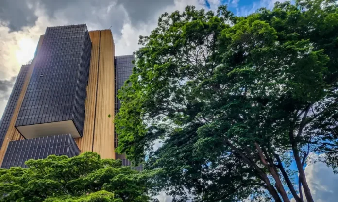 BC lança Protege+ para barrar abertura de contas fraudulentas Edifício sede do Banco Central do Brasil em Brasília, visto de baixo, ladeado por árvores.