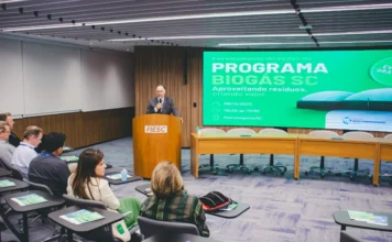 Biogás de SC tem potencial para reduzir emissões Homem de terno discursa em um púlpito com o logo da FIESC, tendo ao fundo um telão verde com a inscrição "Programa Biogás SC".