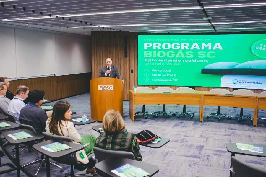 Biogás de SC tem potencial para reduzir emissões Homem de terno discursa em um púlpito com o logo da FIESC, tendo ao fundo um telão verde com a inscrição