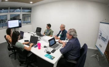 COP30 cria Coalizão Aberta para Mercados de Carbono Reunião em sala de escritório com cinco pessoas sentadas em torno de uma mesa, com notebooks abertos, discutindo a Coalizão Aberta para Mercados de Carbono.