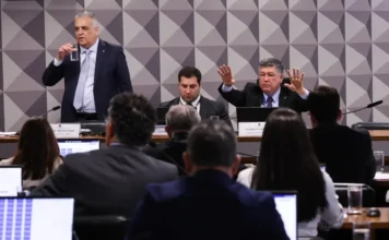 CPMI do INSS convoca governador Romeu Zema para depor Sessão da CPMI do INSS no Senado, com um político em pé (esquerda) e outro gesticulando (direita), e membros da comissão de costas.