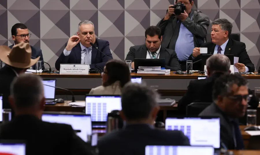 Plenário da CPMI do INSS no Senado, com deputados e senadores em torno de uma mesa, com o relator Alfredo Gaspar em destaque ao centro.