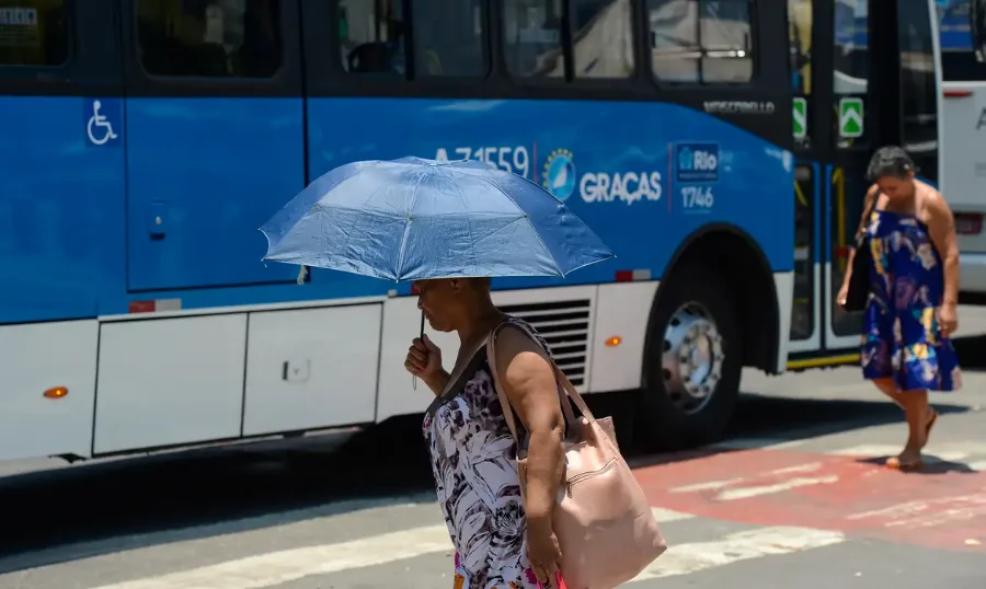 Mulher usa sombrinha para se proteger do sol forte na rua. Alerta de neurocirurgião sobre o aumento de casos de AVC durante o verão devido à desidratação e espessamento do sangue.