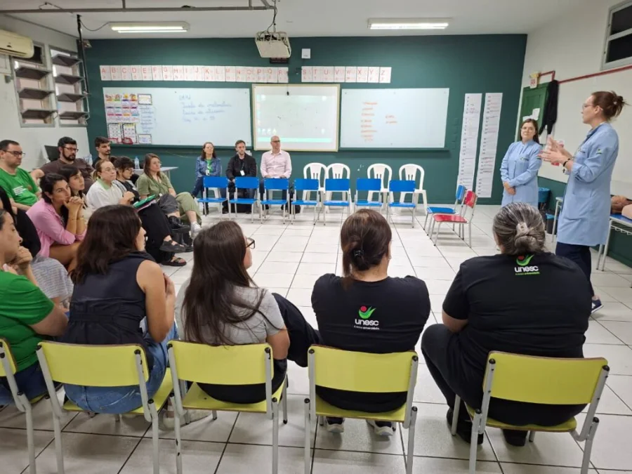 Enfermeira ministra treinamento de primeiros socorros, incluindo a Lei Lucas, para professores e funcionários sentados em sala de aula do Colégio Unesc.