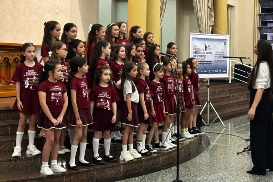 Coral infantil feminino canta em degraus na Catedral São José, com uma maestrina ao lado, durante a abertura do Festival Internacional de Corais.