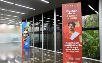 Criciúma inicia campanha Dezembro Vermelho e Laranja Banners da campanha Dezembro Vermelho e Laranja em um saguão, com foco na conscientização sobre HIV/Aids e câncer de pele.