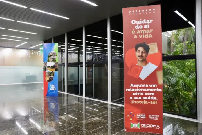 Criciúma inicia campanha Dezembro Vermelho e Laranja Banners da campanha Dezembro Vermelho e Laranja em um saguão, com foco na conscientização sobre HIV/Aids e câncer de pele.