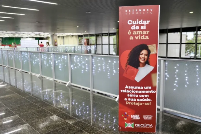 Criciúma realiza mais de mil testes rápidos de ISTs Totem vermelho no Paço Municipal de Criciúma com o texto "Cuidar de si é amar a vida" e a imagem de uma mulher sorrindo; promove a campanha Dezembro Vermelho.