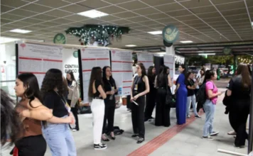 Curso de Contábeis da Unesc reúne alunos em Mostra Científica Estudantes de Ciências Contábeis da Unesc em pé ao lado de banners científicos expostos em um corredor da universidade durante a Mostra Científica.