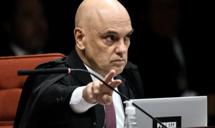 EUA retiram Moraes da lista de sancionados pela Lei Magnitsky O ministro do Supremo Tribunal Federal (STF), Alexandre de Moraes, em plano de close-up no plenário. Ele é um homem calvo, veste toga preta sobre uma camisa social e gravata, e aponta para a frente com o dedo indicador direito. Um microfone está posicionado em frente a ele e um notebook está sobre a bancada.