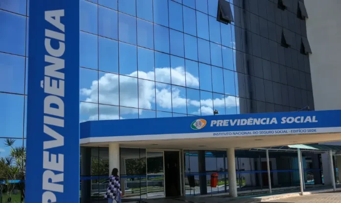 INSS amplia para 60 dias prazo do auxílio por análise documental Fachada de um prédio da Previdência Social em um dia de sol. O edifício tem uma estrutura moderna, com uma parede envidraçada que reflete o céu azul com nuvens brancas. Na parte superior da entrada, há uma faixa azul com o logotipo e o nome "PREVIDÊNCIA SOCIAL - INSTITUTO NACIONAL DO SEGURO SOCIAL - EDIFÍCIO SEDE". Uma placa vertical azul e alta, à esquerda, exibe a palavra "PREVIDÊNCIA". A imagem ilustra a instituição responsável pela ampliação do prazo do auxílio por análise documental.