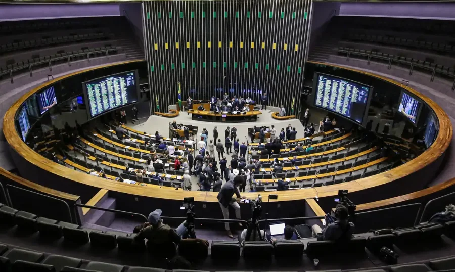 Vista superior do plenário da Câmara dos Deputados durante sessão, mostrando a disposição semicircular das bancadas e painéis de votação.