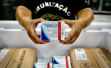 MS inicia distribuição de 673 mil doses de vacina contra VSR Mãos segurando a caixa da vacina contra o Vírus Sincicial Respiratório (VSR) dentro de uma caixa térmica de distribuição.