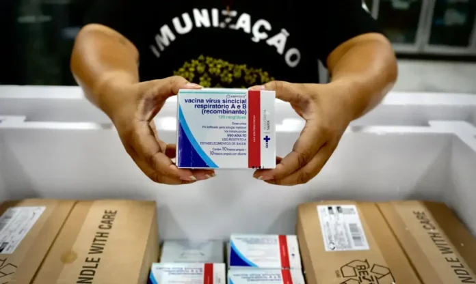 MS inicia distribuição de 673 mil doses de vacina contra VSR Mãos segurando a caixa da vacina contra o Vírus Sincicial Respiratório (VSR) dentro de uma caixa térmica de distribuição.