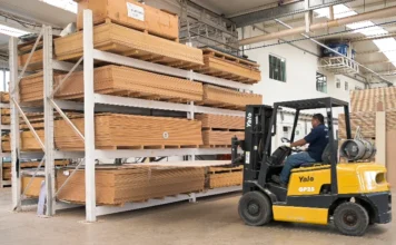 Madeira de SC e Sul é privada, diz FIESC ao governo dos EUA Operador de empilhadeira movimenta uma placa de madeira em um depósito industrial, cercado por grandes estantes metálicas repletas de pilhas de madeira processada.