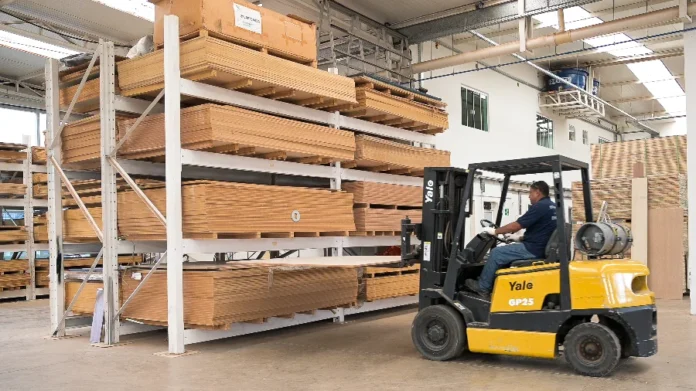 Madeira de SC e Sul é privada, diz FIESC ao governo dos EUA Operador de empilhadeira movimenta uma placa de madeira em um depósito industrial, cercado por grandes estantes metálicas repletas de pilhas de madeira processada.