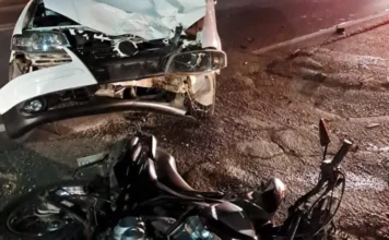 Motociclista tem fratura exposta após colisão em Forquilhinha Vistas noturnas da frente danificada de um carro branco (Volkswagen Gol) e de uma motocicleta preta deitada no asfalto após colisão frontal.