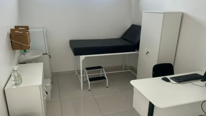 Nova UBS no Arapongas reforça atenção básica em Araranguá Olá! Ótima notícia sobre o avanço na saúde básica de Araranguá com a entrega da nova UBS do Arapongas. Aqui estão as opções de Texto Alt (Texto Alternativo) para a foto do consultório da nova UBS: Opção 1 (Recomendada - Descritiva e Funcional): "Interior de um consultório médico de uma Unidade Básica de Saúde (UBS) recém-inaugurada. O ambiente é claro, com paredes brancas e piso claro. O mobiliário é predominantemente branco e inclui uma maca preta, uma escadinha de dois degraus, uma mesa de trabalho com computador e teclado, e um armário vertical. À esquerda, há uma pia pequena com torneira e dispensador de álcool em gel.