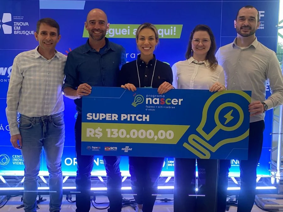 Pain Cave Academy conquista 3º lugar em Super Pitch Day Quatro empreendedores e a representante da Pain Cave Academy posam juntos, segurando um cheque gigante de R$ 130.000,00 do Programa Nascer.
