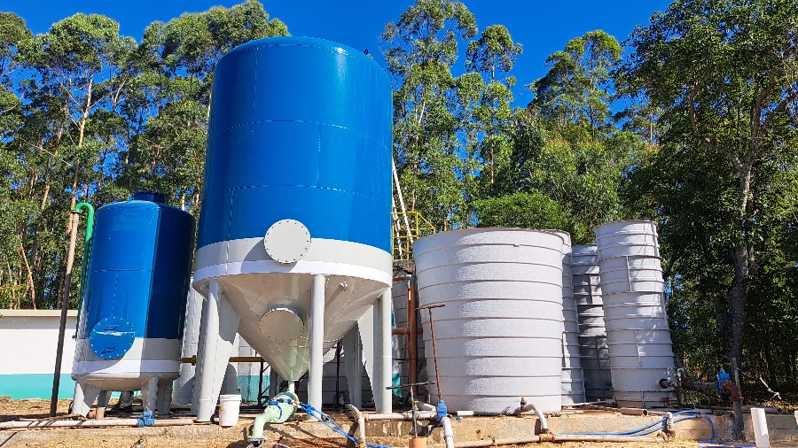 Grandes reservatórios de água azuis e brancos, incluindo um tanque cilíndrico de aço, instalados em meio a árvores na estação de tratamento da Casan em Passo de Torres.