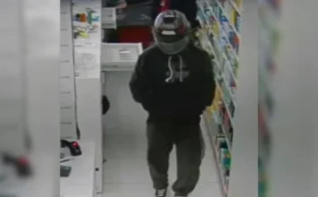 Polícia Civil indicia homem por cinco assaltos em Criciúma Imagem de câmera de monitoramento mostrando suspeito usando capacete e blusa escura dentro de uma farmácia.