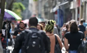 População negra ganha 34% menos em cargos de direção Vista desfocada e movimentada de uma rua central com pessoas caminhando, ilustrando a diversidade da população em um dia de sol.