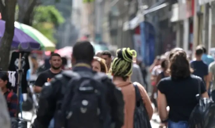 População negra ganha 34% menos em cargos de direção Vista desfocada e movimentada de uma rua central com pessoas caminhando, ilustrando a diversidade da população em um dia de sol.