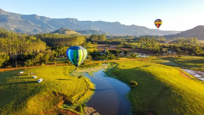 Praia Grande é 1ª no país a concluir regulamentação de balões Vista aérea panorâmica de Praia Grande com dois balões de ar quente flutuando sobre um vale verde e um rio, com montanhas e cânions ao fundo.