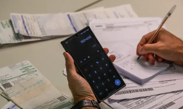Reforma Tributária 2026 será ano de testes e sem multas Pessoa calculando impostos com celular e papel. Receita Federal confirma que o primeiro trimestre de 2026 terá caráter educativo para o IBS e CBS, sem punições para empresas e MEIs que cometerem erros no preenchimento das notas fiscais.