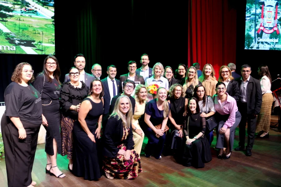 Gisele Silveira Coelho Lopes (reitora) e grupo de líderes e colegas posam juntos no palco do Teatro Elias Angeloni, celebrando a Cidadania Benemérita.