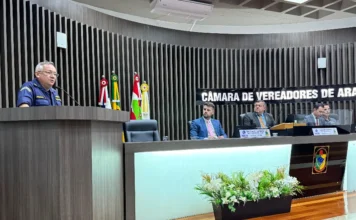Rio Araranguá: Vereadores debatem segurança e regulamentação Capitão de Corveta da Marinha, uniformizado, discursa no púlpito da Câmara de Vereadores de Araranguá durante sessão, com a mesa diretora e bandeiras ao fundo.