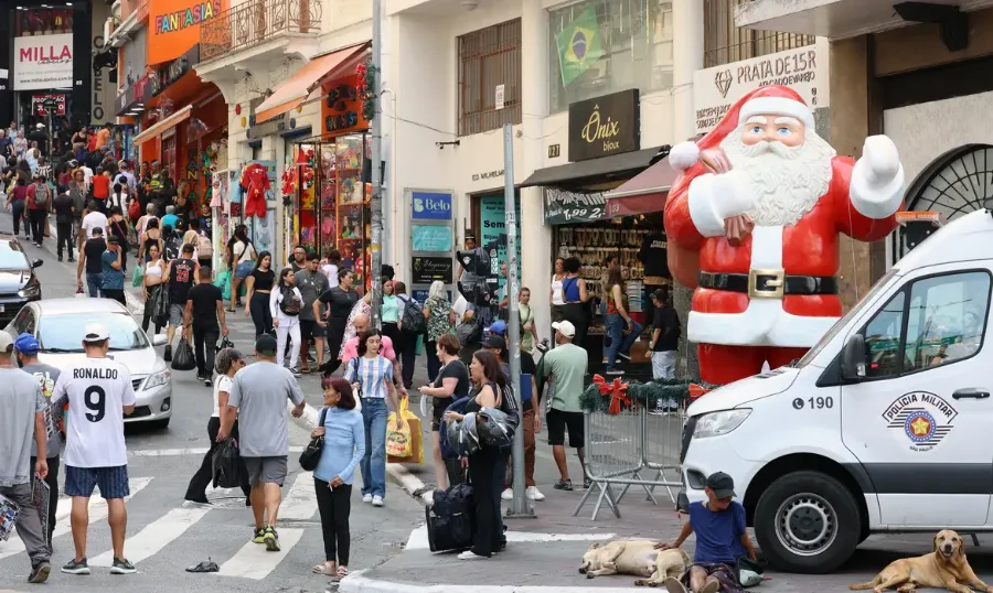 Rua de comércio popular com Papai Noel inflável. Governo Federal oficializa aumento do salário mínimo para R$ 1.621 em 2026, garantindo ganho real acima da inflação para 62 milhões de brasileiros.