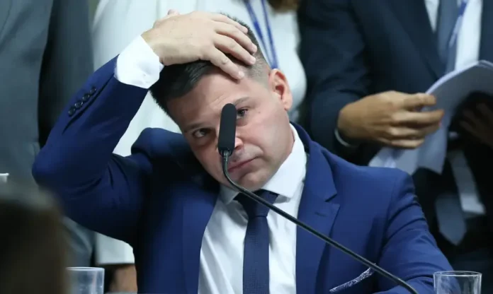 Silvinei tentou fugir do país com passaporte falso Close-up do ex-diretor da PRF Silvinei Vasques em um depoimento, vestindo terno azul e com a mão esquerda sobre a cabeça em sinal de preocupação.