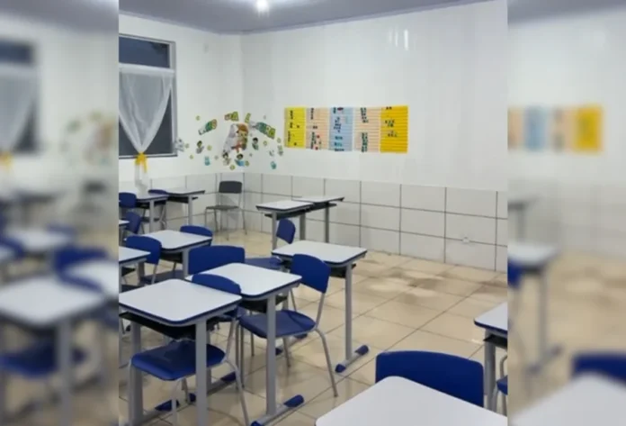 Temporal atinge Balneário Gaivota e deixa casas destelhadas Interior de uma sala de aula de escola em Balneário Gaivota após ser atingida por temporal. As carteiras e cadeiras azuis e brancas estão dispostas em fileiras sobre o piso manchado de água barrenta e suja, que alagou a sala. As paredes são brancas e há sinais de umidade ou sujeira na parte inferior.