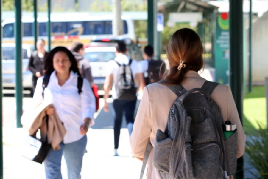 Estudantes caminhando no campus da Unesc com mochilas, em plano desfocado, representando o ambiente universitário.
