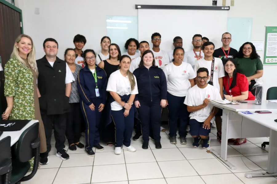 Grupo de alunos com deficiência e professores da Unesc posam para foto em uma sala de aula de informática após a formatura do curso 