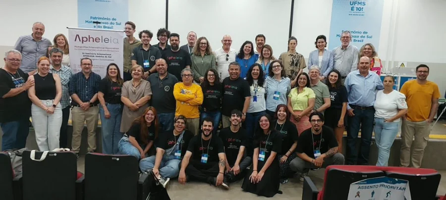 Unesc participa de seminário internacional com 7 países na UFMS Grande grupo de pesquisadores e professores posando para foto em um auditório, com banners do evento Apheleia e da UFMS ao fundo.