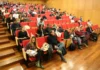 Unesc representa Brasil em Portugal sobre IA e saúde mental Auditório em formato de anfiteatro na Universidade do Minho, em Portugal, lotado de participantes sentados em fileiras de cadeiras vermelhas em degraus de madeira. Vários participantes estão utilizando notebooks no colo e alguns fazem anotações, acompanhando a palestra sobre Direito e Tecnologias Digitais.