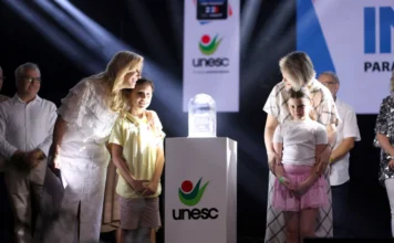 Unesc vence prêmio de “Lugares Mais Incríveis” pela 4ª vez Reitoras e duas crianças em um palco iluminado, ao lado de um troféu de vidro sobre um pedestal com o logo da Unesc, após a premiação "Lugares Mais Incríveis para Trabalhar".