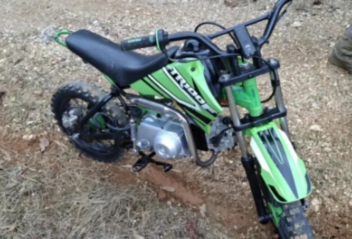 Urussanga Adolescente cai de mini-moto ao fugir da PM (1) Fotografia de uma mini-moto de 50 cilindradas, modelo TRX, nas cores verde e preta, caída sobre uma estrada de terra e brita. O veículo apresenta pneus de cravos sujos de lama e guidão preto. Ilustra a apreensão em Urussanga.