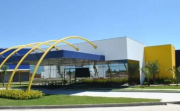 ACIVA celebra chegada da Baly e expansão em Araranguá Fachada moderna da unidade industrial em Araranguá, destacando painéis de vidro espelhado, detalhes em amarelo e azul na arquitetura e estrutura metálica curva. A área externa possui gramado e palmeiras, representando as futuras instalações da Baly Brasil Energéticos no município.