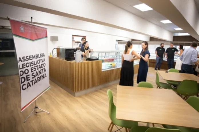 ALESC e Senac iniciam operação de restaurante-escola Fotografia do ambiente interno da nova lanchonete no Palácio Barriga Verde, exibindo balcões de atendimento, funcionários do Senac uniformizados e clientes em um espaço moderno e iluminado.