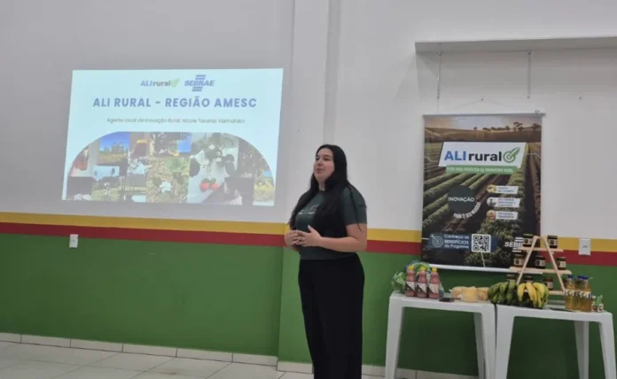 ALI Rural reúne produtores da AMESC em Santa Rosa do Sul Palestrante apresenta o programa ALI Rural - Região AMESC durante encontro com produtores rurais em Santa Rosa do Sul; ao lado, banner do programa e mesa com produtos agrícolas locais.