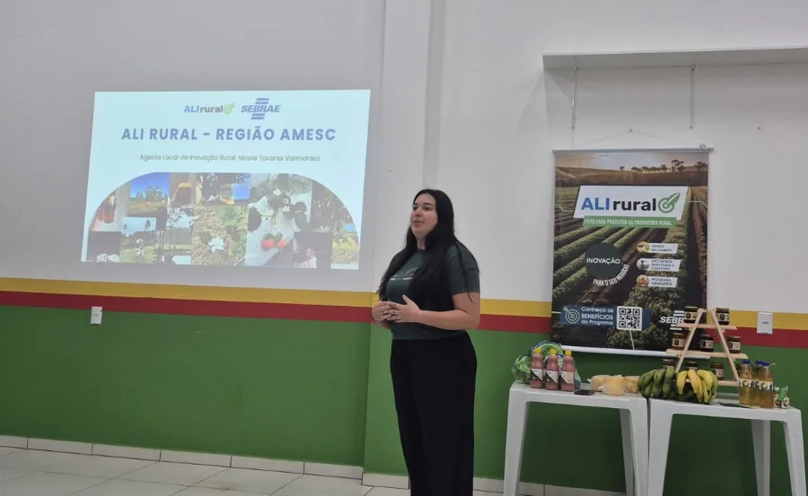 Palestrante apresenta o programa ALI Rural - Região AMESC durante encontro com produtores rurais em Santa Rosa do Sul; ao lado, banner do programa e mesa com produtos agrícolas locais.