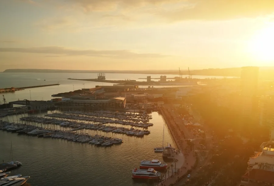 Acordo Mercosul-UE Sebrae vê chances para PMEs de SC Vista aérea panorâmica de uma cidade costeira com uma grande marina repleta de barcos e uma área portuária ao fundo, banhada pela luz dourada do pôr do sol, ilustrando o cenário logístico e as conexões do comércio internacional debatidas na matéria sobre o acordo Mercosul-UE.
