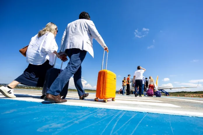 Aeroportos de SC batem recorde histórico de passageiros "Passageiros com malas caminham pela pista de um aeroporto em Santa Catarina em direção a uma aeronave, ilustrando a movimentação recorde de 8,5 milhões de viajantes no estado em 2025."