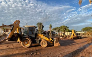 Alesc foca em clima e proteção animal em 2025 Retroescavadeiras trabalham na limpeza e remoção de lama e destroços em via pública após uma enchente, ilustrando a importância da nova legislação catarinense que facilita o intercâmbio de máquinas e auxílio entre municípios em situações de desastres naturais.