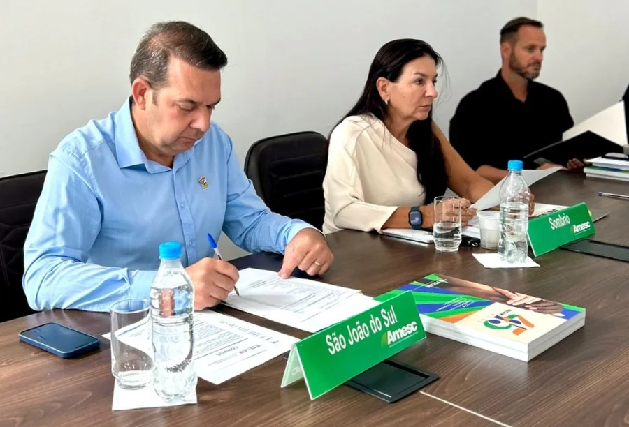 Novo presidente da Amesc, Alex Bianchin (São João do Sul), assina termo de posse durante assembleia, sentado ao lado da prefeita de Sombrio, Gislaine Cunha.